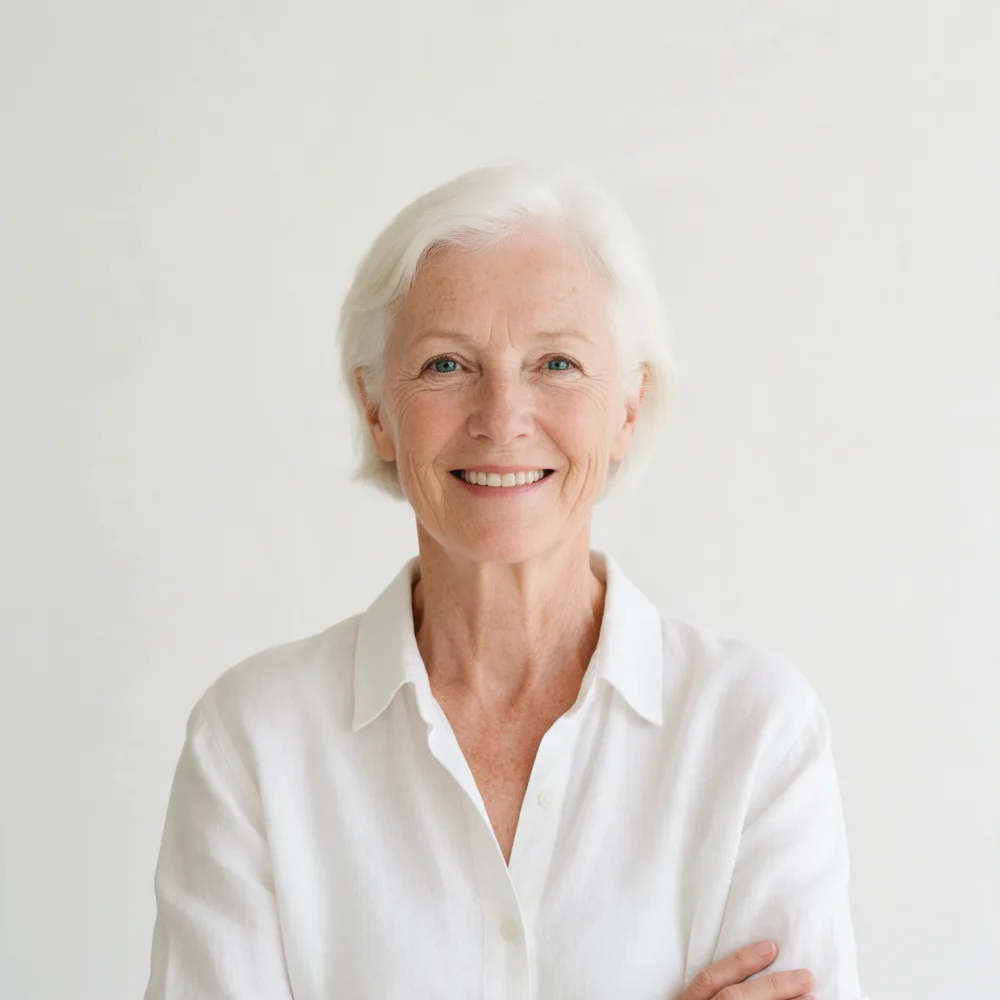 Smiling woman with short white hair in a white linen shirt, arms crossed